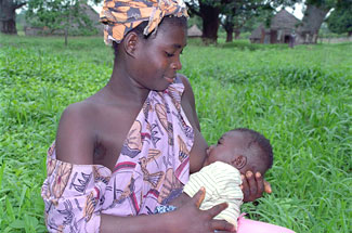 A young African woman sits and breastfeeds her baby.
