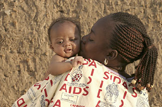 An African mother holds her baby on her shoulder; the mother's shirt is printed with AIDS prevention messages.