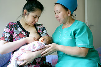 A new mother is shown how to breastfeed by a nurse.