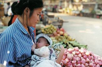 A mother breastfeeds as she tends her produce market stall.